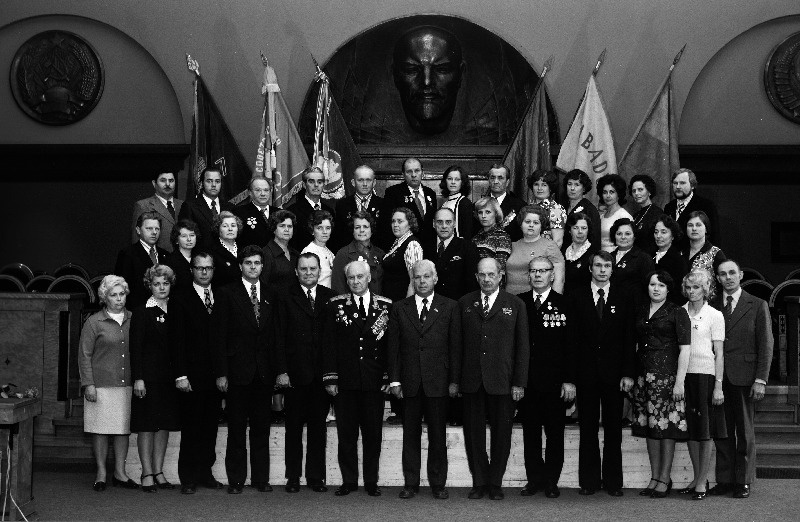 Vabariigi töötajate, sotsialistliku võistluse võitjate pildistamine revolutsiooni-, lahingu - ja töökuulsuse lippude juures Eesti NSV Ministrite Nõukogu Valges saalis seoses Suure Sotsialistliku Oktoobrirevolutsiooni 60. aastapäeva tähistamisega, Eesti NSV MN juures asuva Statistika Keskvalitsuse vanemökonomist Õie Kangur, Eesti Vabariikliku Valitsuse Estelektrokomplektsnab elektritõstuki juht Ülo Allik, Haapsalu Rajooni TSN Täitevkomitee Rahandusosakonna juhataja Hans Šeripov, Eesti NSV MN juures asuva Statistika Keskvalitsuse Võru Rajooni Informatsioonijaama ülem Maret Danileiko,    jätkub: Eesti NSV MN Riikliku Plaanikomitee osakonnajuhataja Viktor Stepanov, Mererajooni Rahvakohtu rahvakohtunik Nikolai Sudak, Eesti NSV Sideministeeriumi juures asuva sõjaväestatud rühma ülem Petr Smirnov, Eesti NSV Sideministeeriumi N asutuse autojuht Boris Mutonin, NSV Liidu Riigipanga EV Kontori Linna Valitsuse vanemökonomist Pilvi Otstaavel, Eesti NSV Siseministeeriumi Ehitu