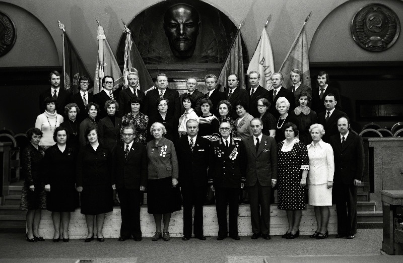 Eesti NSV Haridusministeeriumi süsteemi asutuste töötajate, sotsialistliku võistluse võitjate pildistamine revolutsiooni-, lahingu - ja töökuulsuse lippude juures Eesti NSV Ministrite Nõukogu Valges saalis seoses Suure Sotsialistliku Oktoobrirevolutsiooni 60. aastapäeva tähistamisega, pensonär, sotsialistliku töö kangelane Leida Soovik, Tallinna Linna Mererajooni TSN Täitevkomitee Haridusosakonna metoodik, Eesti NSV teeneline õpetaja Eha Sillam, Tartu 7. Keskkooli õpetaja, Eesti NSV teeneline õpetaja Hans Pukk, Tallinna 6. Keskkooli õpetaja, Eesti NSV teeneline õpetaja Veniamin Smirnov, Tapa 1. Keskkooli vanemõpetaja,    jätkub: Eesti NSV teeneline õpetaja Õilme Oglas, Loksa Keskkooli direktor, Eesti NSV teeneline õpetaja Robert Adamson, Rapla Keskkooli direktori asetäitja õppetöö alal, Eesti NSV teeneline õpetaja Laine Kilusk, Põlva Keskkooli õpetaja, Eesti NSV teeneline õpetaja Tiiu Kiudorv, Tallinna 39. Keskkooli direktor, Eesti NSV teeneline õpetaja