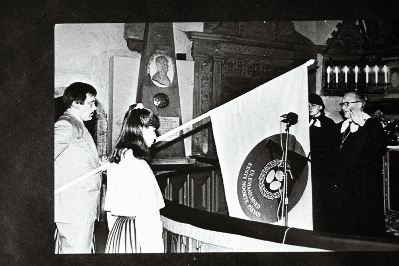 I ülemaailmsele eesti noorte päevade lipu õnnistamine Toomkirikus. Lippu hoiab ürituse peakorraldaja Henno Selirand ja tseremooniat viib läbi Tartu praost Harald Tammur.