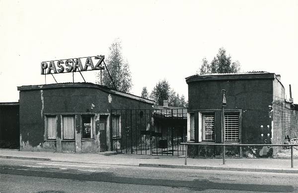 Foto. Ringpoe Passaaž Narva mnt poolne külg ( arh. A. Matteus, 1938). Reklaamsilt katusel; metallvärav.
Tartu, 1990. Foto: Harri Duglas.