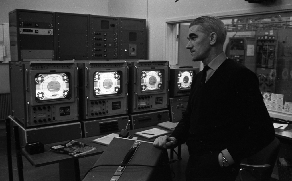 Lockhyttan, Vinfest "Drotten" 23 mars 1967

En man klädd i svart kostym, vit skjorta och svart slips står inne i Radio- och TV-masten Lockhyttan. Han befinner sig iett rum med TV-apparater och teknisk utrustning.