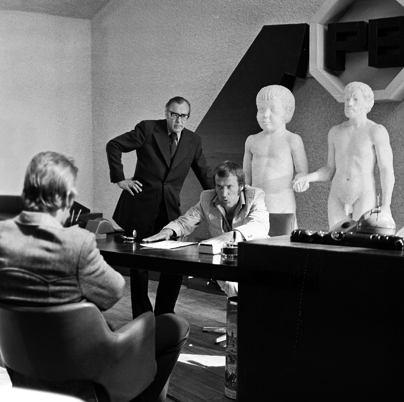 Tallinnfilmi mängufilmi "31. osakonna hukk" I seeria. Seisavad Jensen (Lembit Ulfsak) ja I direktor (Heino Mandri), istub kirjastaja (Ago Roo). Kaadris Ülo Õuna skulptuur "Isa ja poeg".