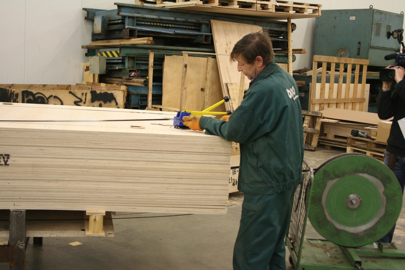 Pakendamisprotsess OÜ Baltic Panel Groupis, töötaja kinnitamas metallribaga vineertahvleid.