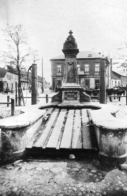 Henningi plats : kaunistustega postament (arvatav verstaposti tähis), millel on aastaarv 1882.  Kummalgi pool postamenti on pumbakaev.

Taga on ärihoone Fortuuna, Holmi, Raatuse ja Peterburi t ristumiskohal. Ärihoonel  reklaamsilt: Rohu ja wärwi kauplus. Voorimehed. 

Tartu, ca 1914.  duplicate photo