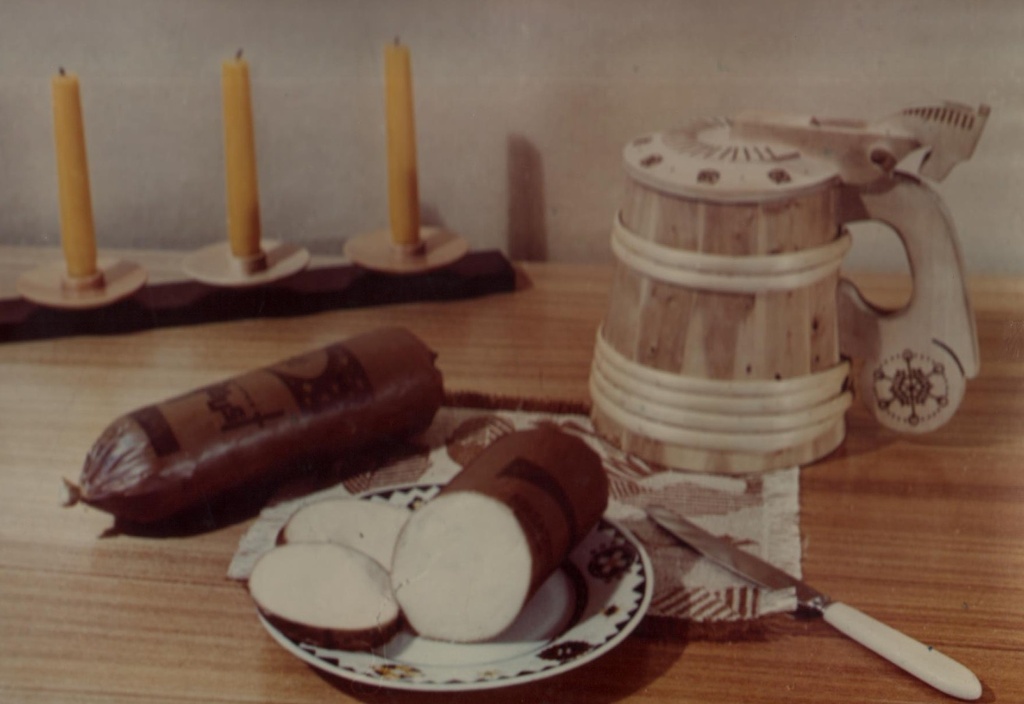 Lauakujund: sulatatud vorstjuust taldrikul, laual suveniir õllekapp; tagaplaanil küünlad