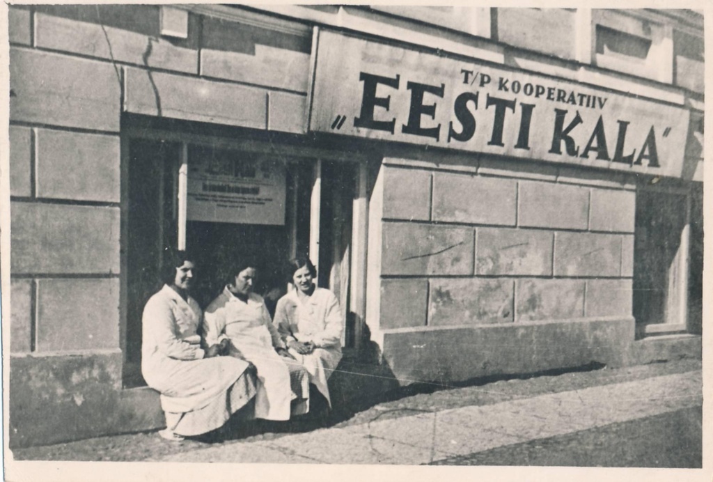 Kalakauplus Politseiplatsi ääres. 3 heledas töökitlis naist poe akna juures.  Majal silt T/P kooperatiiv "Eesti kala".  Tartu, 1928.