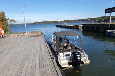 Retkeläiset menossa taksiveneeseen Vallisaaressa. Paikka on Torpedolahden laituri Vallisaaren itärannalla. Taivaanrannassa Haminansalmen toisella puolen näkyy Santahamina. rephoto