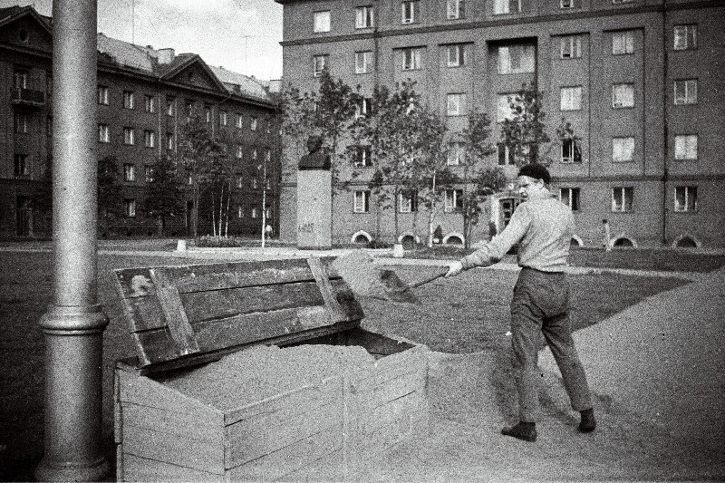 Heakorratööline täidab J. Anveldi tänava haljasalal kasti liivaga, tagaplaanil kommunistliku tegelase ja kirjaniku Jaan Anveldi mälestussammas.