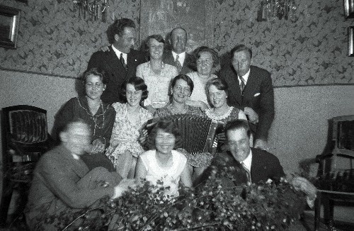 Kaksteist inimest grupipildil. Keskel naine akordioniga