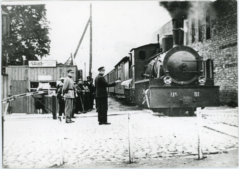 Kitsarööpmeline reisirong auruveduriga Uk 81 Tallinnas Tartu maantee ülesõidul, lahtise rohelise lipuga ülesõiduvaht annab signaali "tee on vaba", 1930