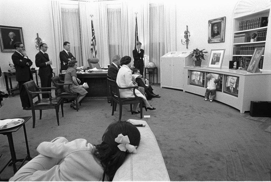 LBJ White House a7160-16a - President Lyndon B. Johnson, family members, and staff watching the President's announcement of bombing halt on television
President Lyndon B. Johnson, family members, and staff watch the President's address on three televisions. Grandson Patrick Lyndon Nugent, wearing his Halloween costume, plays in front of them.