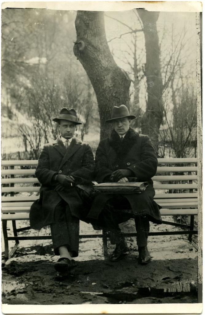 Kaks meest pargipingil istumas, mantlites ja kaabudega.