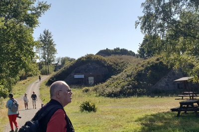 Näkymä Vallisaaren linnoituksilta saaren luoteisrannikolla. Maastoon on rakennettu kiviseinäisiä ruutivarastoja, jotka venäläiset rakensivat 1860-1870-luvuilla. Ne on katettu maakerroksella, ja ne saavat maaston kumpuilemaan. Hiekkainen kävelytie kiemurtelee kumpujen välistä. Vasemmalla näkyy holvikaarimainen betoninen sisäänkäynti varastoon. rephoto