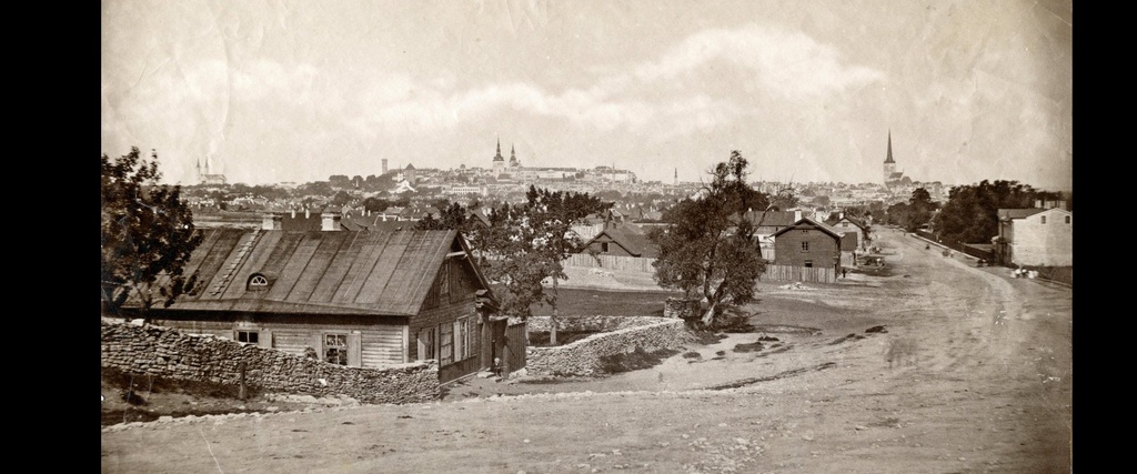 Paremal heleda otsaseinaga praegune Tartu maantee 73, (valmis 1881, arh Nikolai Thamm, 1900ndate alguses saanud juurde- ja ümberehituse) Brandmanni saunana tuntud elu- ja ärihoone (Tartu maantee saun).
✅ Järgmisena, puudesalust paistmas selle kandi üks vanemaid puithooneid, Tartu mnt 69. Oliver Orro sõnul üks piirkonna vanimaid hooneid, asustus- ja linnaehitusajaloolise väärtusega kui haruldane näide Tartu postimaantee vanast, praegusele kihistusele eelnenud hoonestusest. Üksikehitisena huvitav Tallinna puitarhitektuuris ainulaadse külgfassaadi galeriiveranda tõttu. 1856 a kaardil maja kenasti olemas, kinnituregistris on esimene saadaolev sissekanne 29.05.1864, kui kinnistu omandas tisler Conrad G. Sporleder.
*Kas vasakul, praeguse Odra-Lastekodu ristil näha olev kaarakendega kivimaja võib olla Lastekodu 31, kunagise Düüna rügemendiga seotud hoone?
✅ Aga mäest alla vasakul tänapäeval muidugi Liviko kompleks, piiritulp tundub olevat tänase Odra tn otsa kohal.