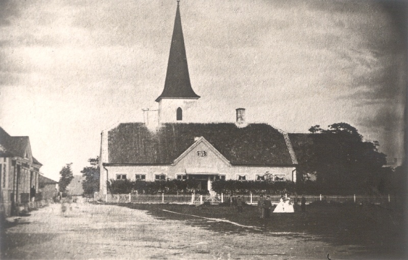 Foto. Haapsalu raekoda ja Kooli tänav. Tagaplaanil Jaani kirik. Esiplaanil mõned inimesed muruplatsil, kuhu 1883-1886 istutati park. Foto u 1880.