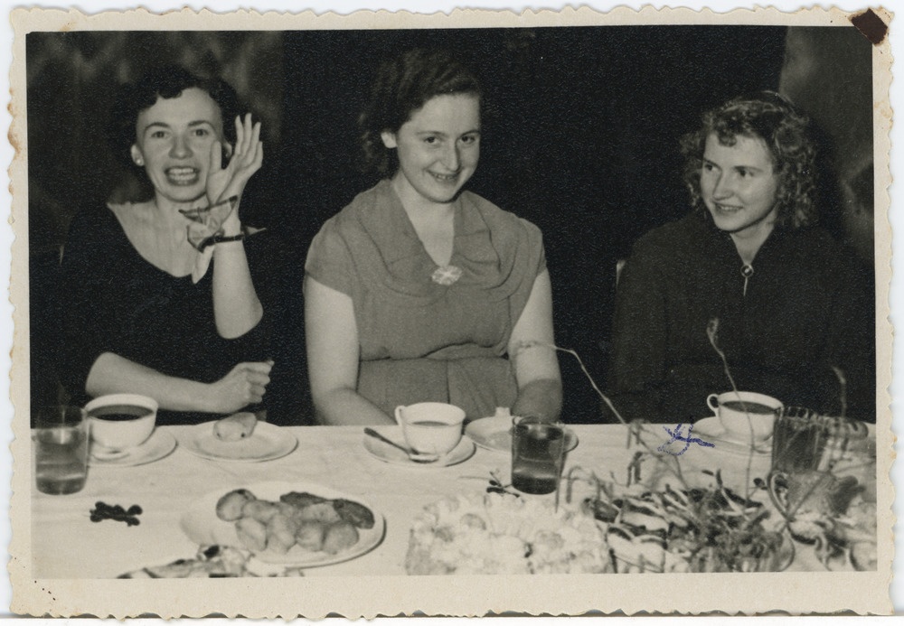 Kolm neiut kaetud lauataga istumas