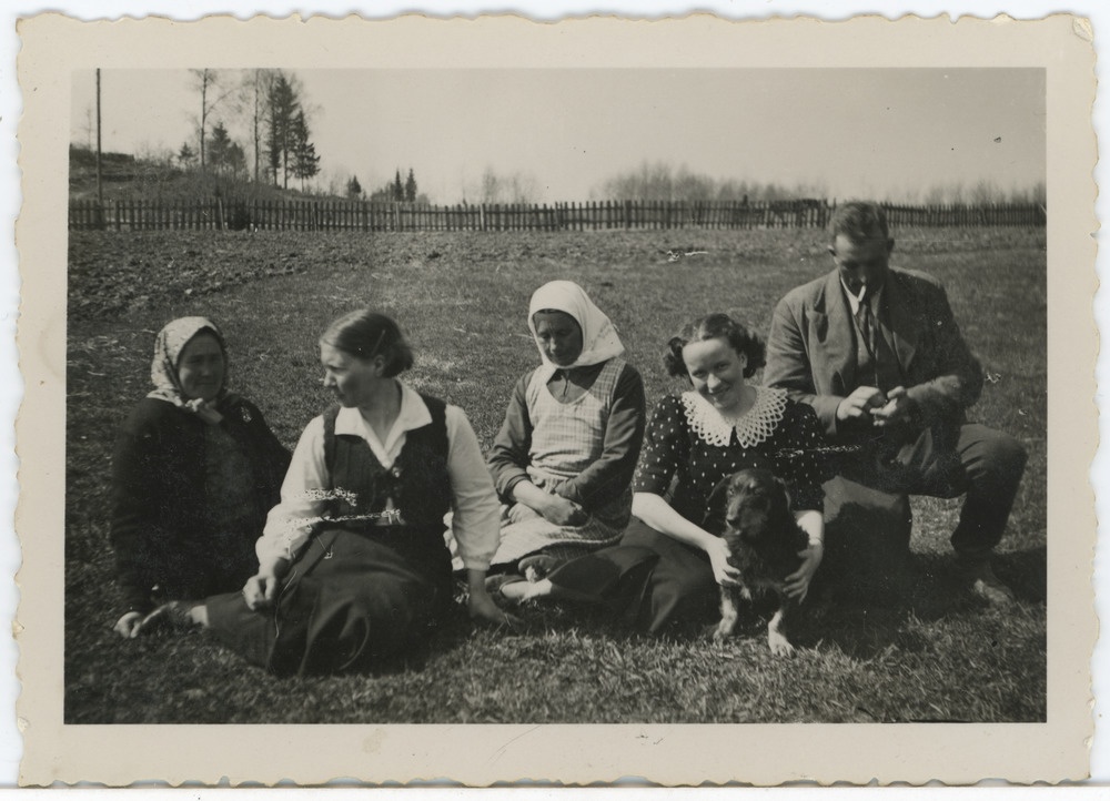 Grupp inimesi maastikul istumas, paremalt teine Salme Maling (Maimre, Ümarik) koos koeraga