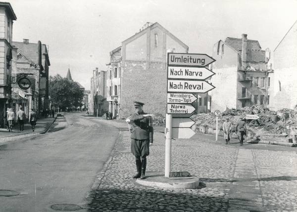 Tartu varemed. Võidu (Promenaadi) ja Uueturu t nurk: Eesti ohvitseri (või Eesti Omakaitse) mundris mees liiklust reguleerimas.
Teeviit arvukate kirjadega (Umleitung. Nach Narva. Nach Reval. Wesenberg - Torma - Taps. Narwa. Tschernyj). Taga teeviit kirjaga Feldwerkstoff.
Vasakul nn Tillemanni kell, taga Jaani kiriku torn.
Tartu, 29.08.1941.