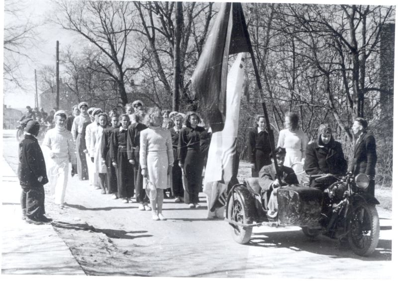 Foto. Sportlased 1. mai rongkäigus Haapsalus. Esiplaanil külgkorviga mootorratas, mille järel nais- ja meessportlased. 1949.