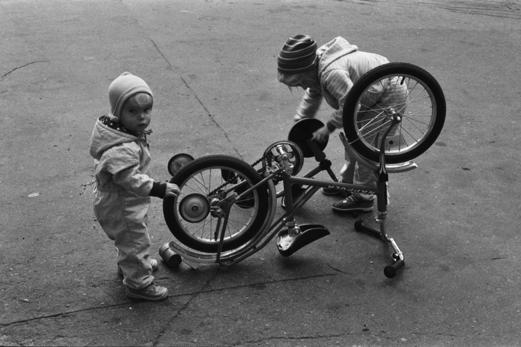 Liisankatu 7. Kaksi lasta ja nurinpäin käännettyä lasten polkupyörää Liisankatu 7:n pihalla. Etualalla Helkaman Nappula-merkinen pyörä.