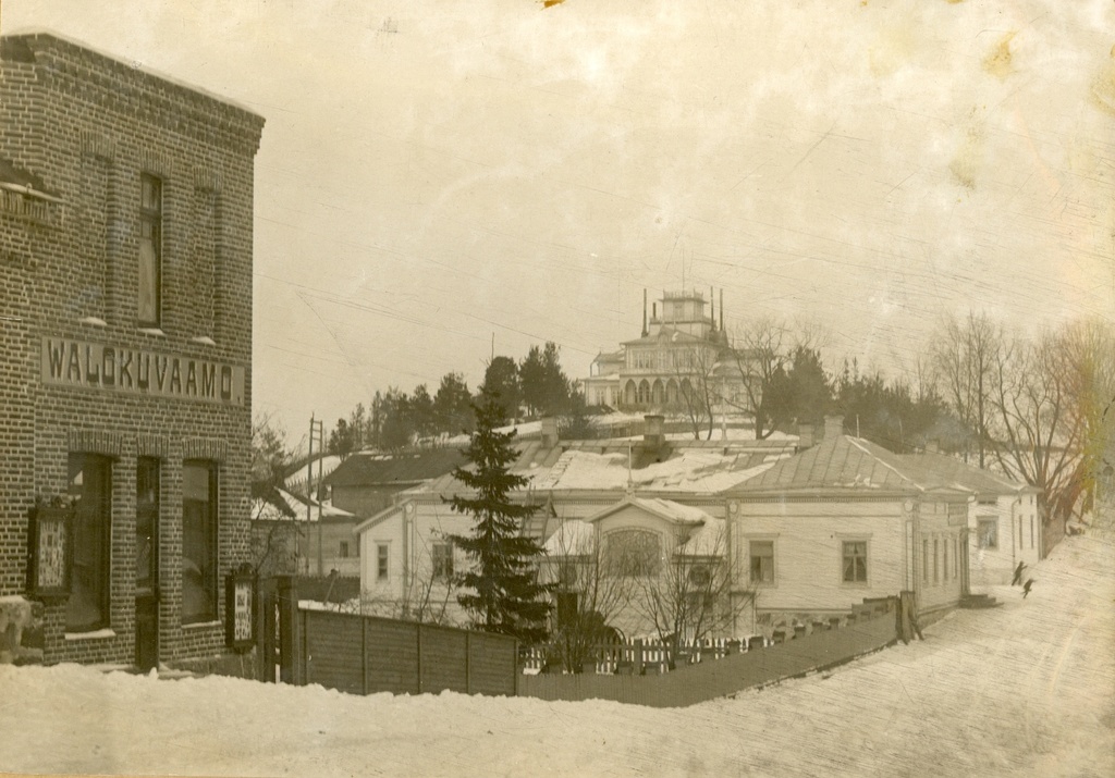 Näkymä Kirkkokadulta koilliseen päin. Kadun vasemmalla puolella tiilirakennus (Kirkkokatu 7), jonka seinässä teksti "Walokuvaamo". Rakennuksessa on toiminut  A. Sihvosen valokuvaamo. Taustalla näkyy Piispanlinna. talvi 1900-luku–1920-luku. View northeast from Kirkkokatu