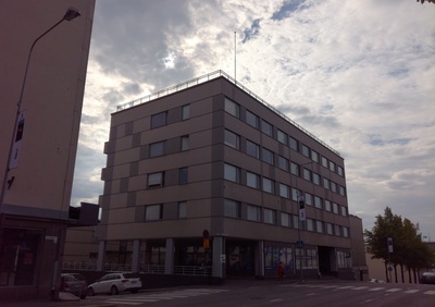 Entinen raatihuone, myöhemmin posti (Olavinkatu 36) idästä Olavinkadun yli. Olavinkatu 34:n kohdalla puuaidassa mainoskaappeja, katu mukulakivipäällysteinen, kangaskattoinen auto, jalankulkijoita. Takana oikealla And. Auvisen rakennus (Olavinkatu 38). rephoto
