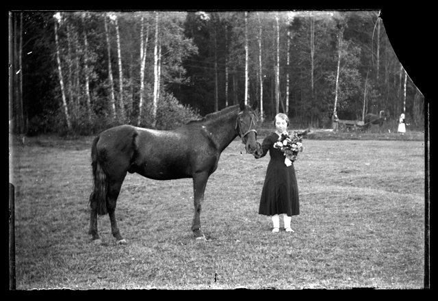 Pidulikus kleidis lilledega tütarlaps hobust päitsetest hoidmas