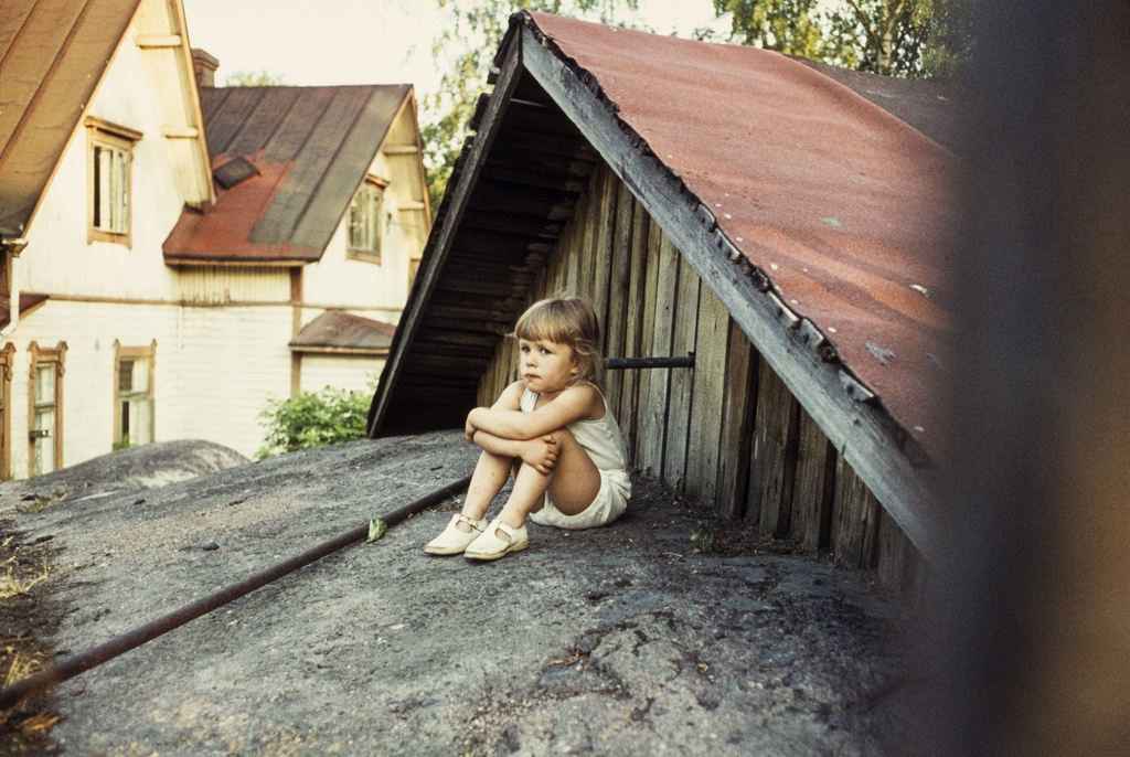 Pikkutyttö istumassa ulkona Hertankatu 5:n pihalla kallioilla Puu-Pasilassa.