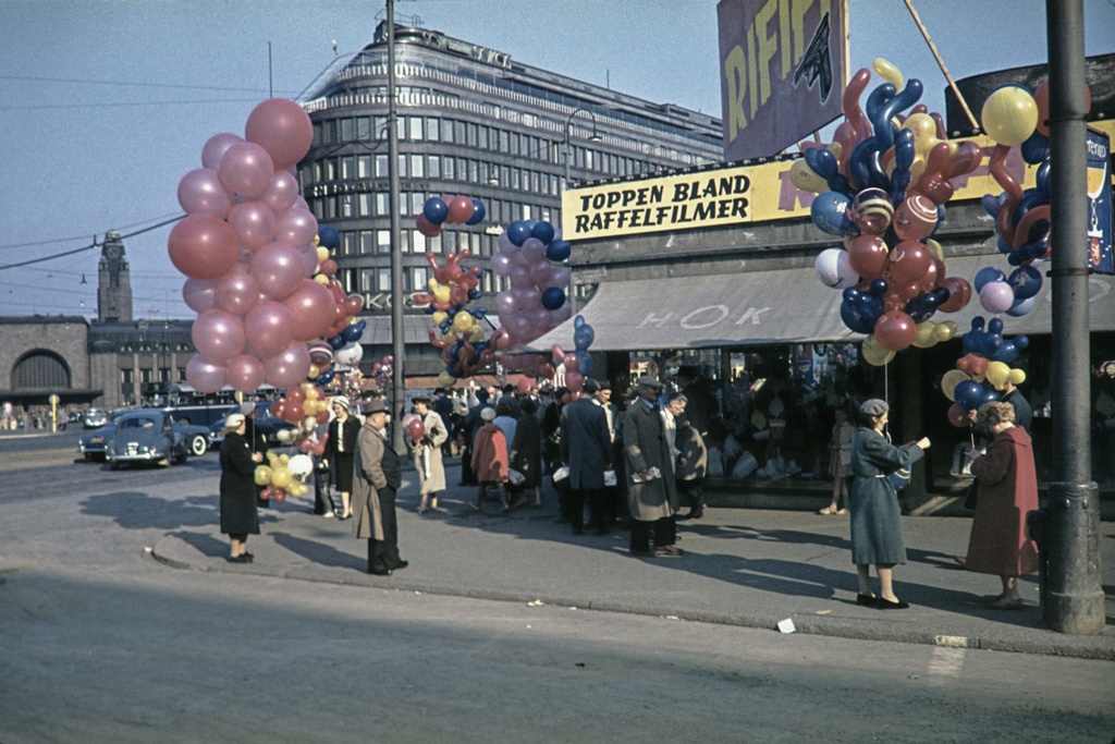 Ilmapallonmyyjiä vappuna Lasipalatsin kulmalla. Mannerheimintie 24 - 22. - Salomonkatu. Taustalla Rautatieasema ja Sokos -tavaratalo, Mannerheimintie 9.