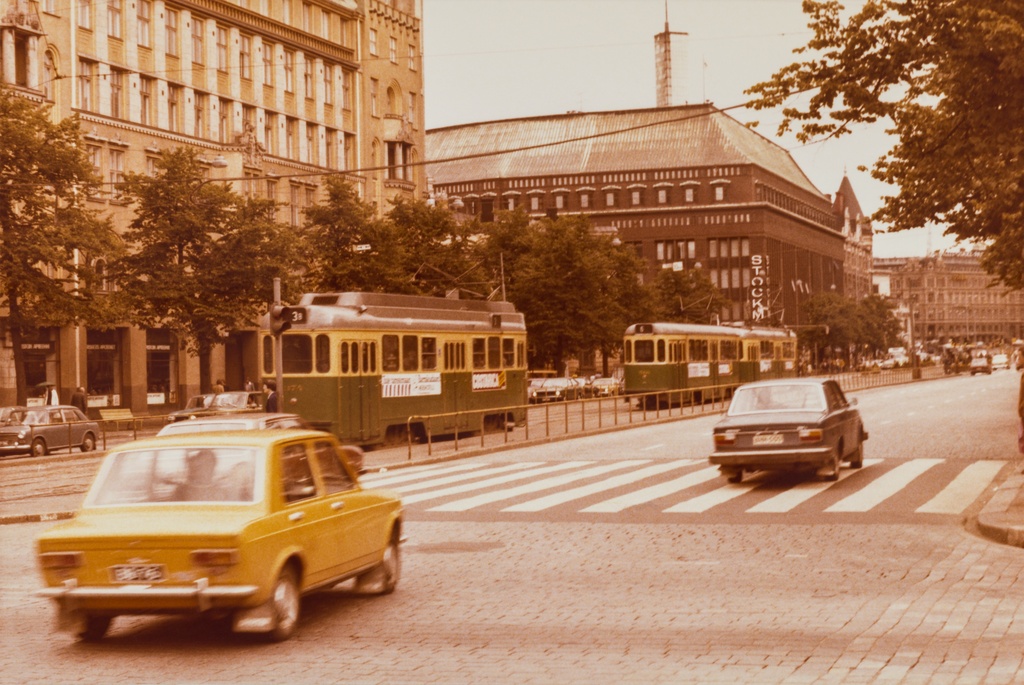 Raitiovaunuja (HKL 374 ja samaan sarjaan kuuluva toinen vaunu) Mannerheimintiellä linjalla 3B ja 6. Taustalla Uusi ylioppilastalo ja Stockmanin tavaratalo, Etualalla autoja ja suojatie.