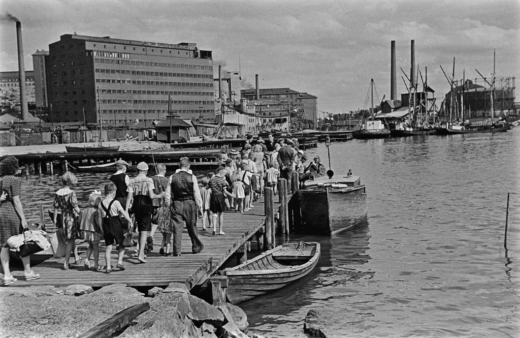 Lapsia laiturilla Sörnäisten rannassa lähdössä Sompasaareen, jossa toimi kesäsiirtola Elannon työntekijöiden lapsille. Taustalla OTK:n mylly sekä Sörnäisten satama- ja teollisuusaluetta.