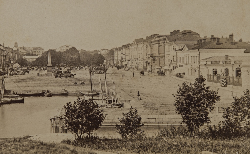 Kauppatori ja Pohjoisesplanadi 1, 3, 5, 7, 9, 11-13. Etualalla Katajanokan Kanavapuistoa, Katajanokan kanavaa ja Linnanallas, johon on kiinnitetty purje- ja soutuveneitä.