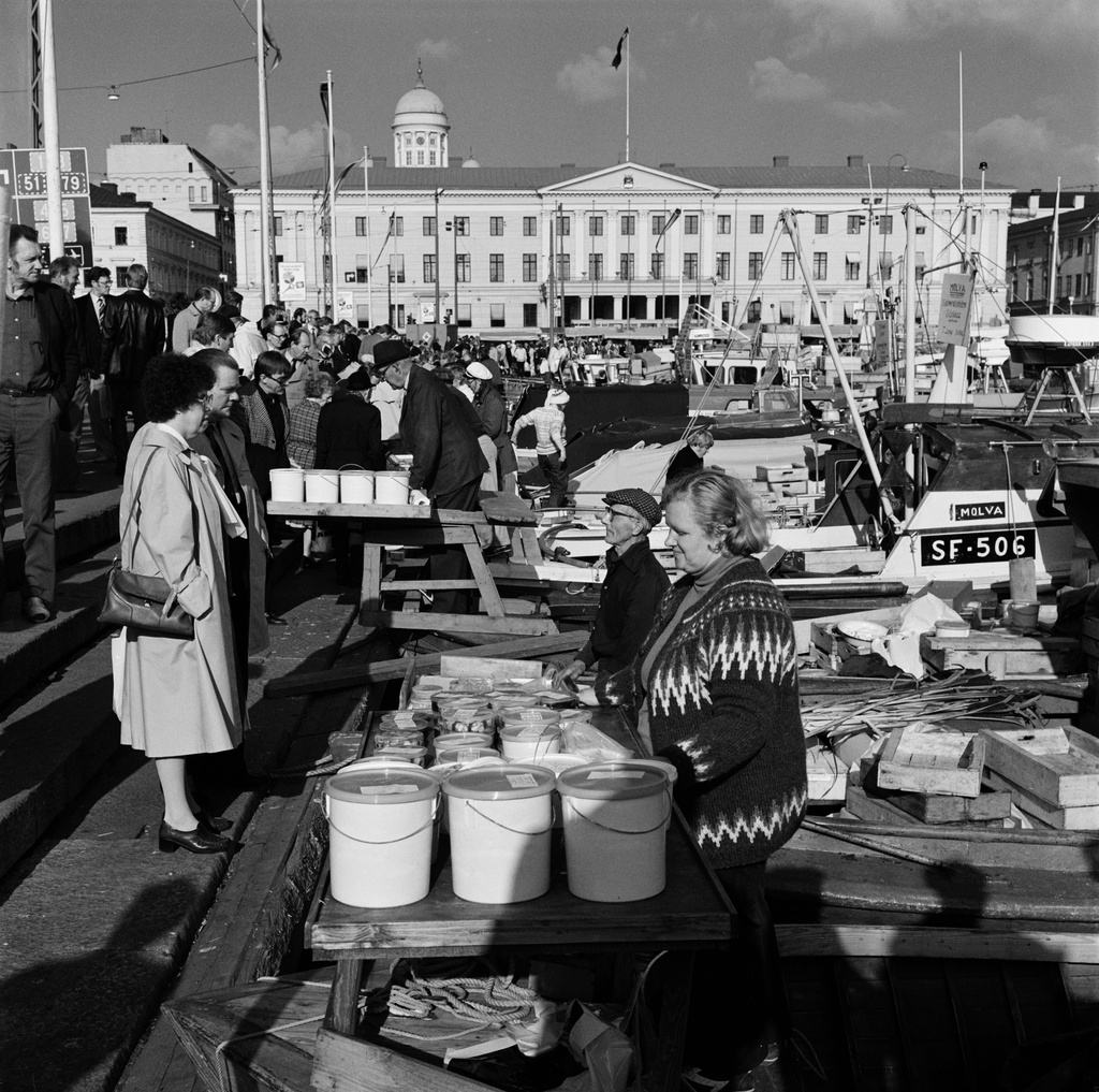 Silakkamarkkinat Eteläsatamassa. Maustettua silakkaa myydään kalastajaveneestä Kolera-altaan reunalla. Taustalla Kaupungintalo, Pohjoisesplanadui 11-13.