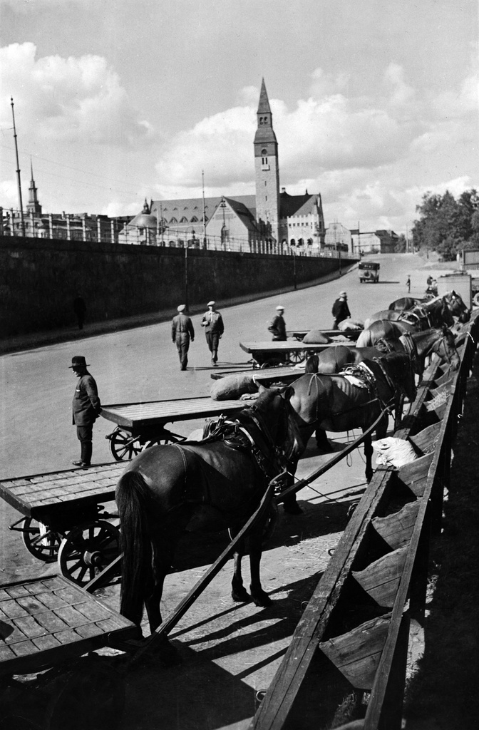 Edessä hevosajureita Ala-Mannerheimintiellä, hevoset seimien äärellä.Taustalla Kansallismuseo, Mannerheimintie 34 (= Turuntie 6). Arkkitehdit Gesellius, Lindgren, Saarinen, avattiin 1916.