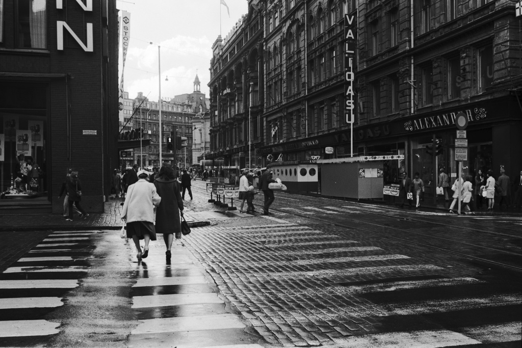 Aleksanterinkatu 19. Näkymä sateen jälkeen kävelykatukokeilun aikoihin Aleksanterinkadulta Keskuskadun risteyksestä Mannerheimintien suuntaan. Vasemmalla Stockmannin tavaratalon kulma, oikealla Hermeksen talo, Aleksanterinkatu 19.