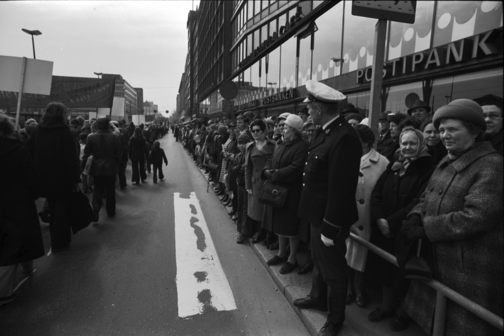 Siltasaarenkatu. Ihmisiä seuraamassa runsain joukoin työväen vappukulkueen liikkeelle lähtöä Siltasaarenkadun laidalla 1.5.1972. Oikealla Postipankin edustalla poliisi. Näkymä etelään Pitkänsillan suuntaan.