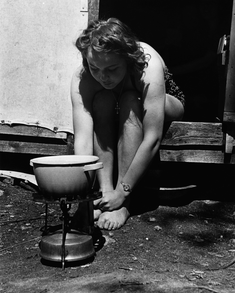 Kivinokka. Nainen uimapuvussa valmistaa ruokaa priimus-keittimellä pahvimökin edustalla.