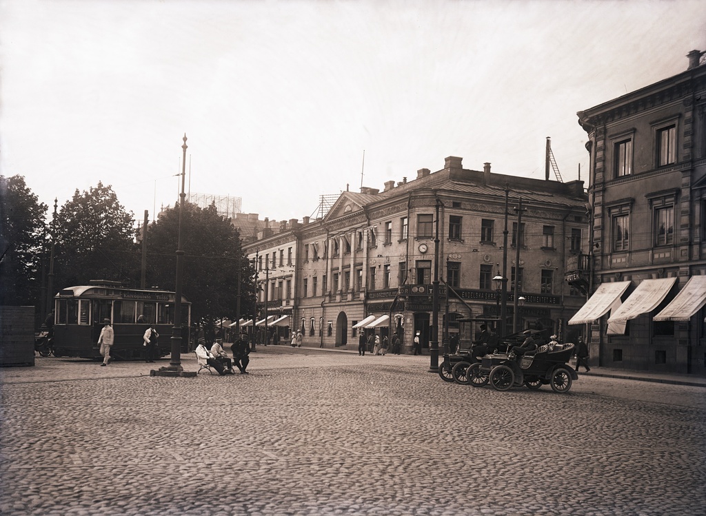 Helsingin ensimmäinen vuokra -autoasema kauppatorin laidalla, Pohjoisesplanadi 19, 21. Edessä Oldsmobile, vieressä osittain katettu Cadillac, molemmat vm 1905. Ensimmäinen taksilupa annettiin 1906.