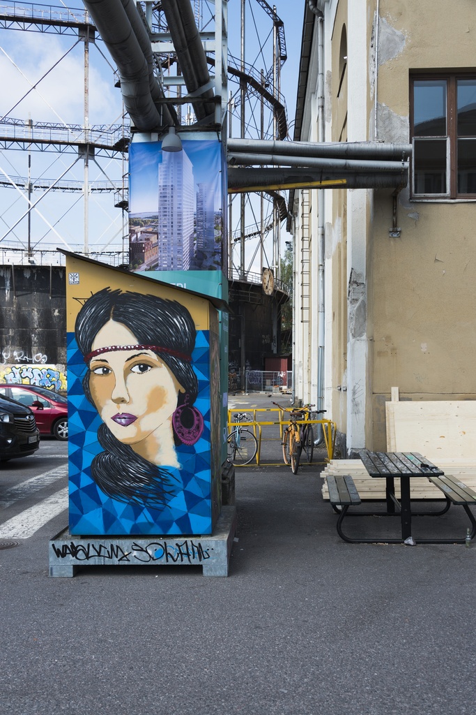 Kalasataman dokumentointi. Suvilahden alue, rakennelma jossa graffiti, naisen muotokuva. Taustalla kaasukello.