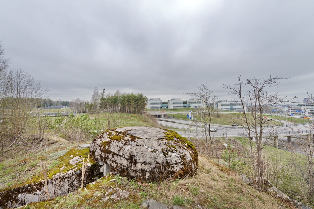 Ruukinranta. Ensimmäisen maailmansodan aikainen maalinnoitus, puolustusasema XXXVI:1 Ruukinrannassa, Espoossa. Kuvassa on linnoitteen länsipäässä sijaitseva soikea, kupukattoinen kivääri- tai tähystysasema. Betonista tehtyyn rakenteeseen johtaa kallioon louhittu hauta, jonka seinät on myös tuettu betonilla. Taustalla näkyy Kehä 1:n ja Turunväylän välinen risteyssilmukka, sekä useita rakennuksia. Kuvaussuunta lähes länteen.