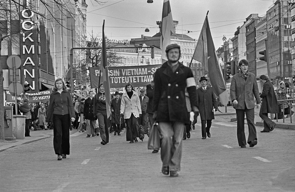 Mielenosoittajia marssimassa ajoradalla Mannerheimintiellä Kolmensepänaukion kohdalla. Mielenosoittajat kantavat Vietnamin sodan vastaisia banderolleja ja lippuja. Takana vasemmalla Stockmannin tavaratalo.