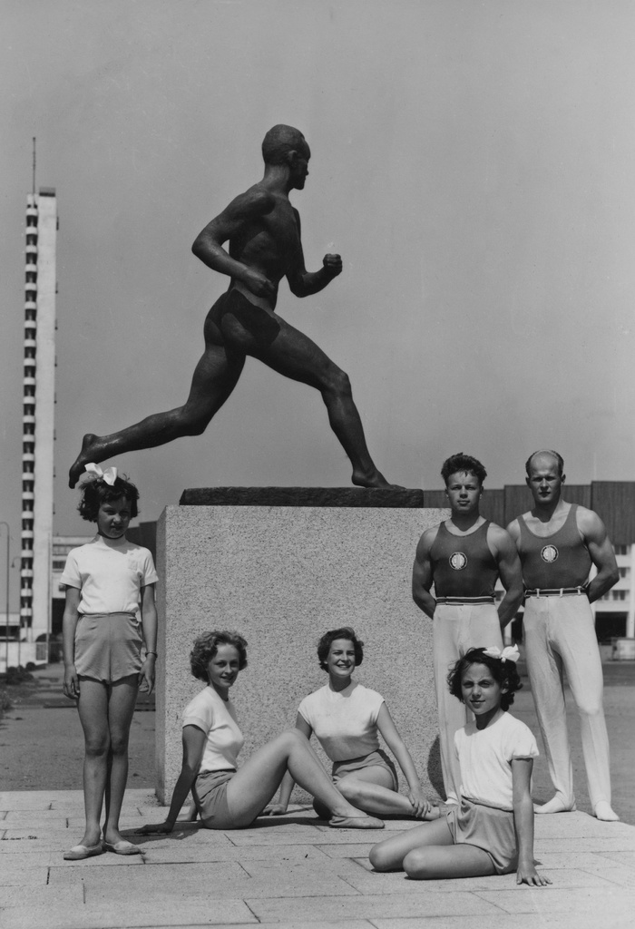 Urheilijoita Paavo Nurmen patsaan edessä olympialaisten aikaan Stadionin etukentällä. Taustalla Olympiastadion ja stadionin torni.