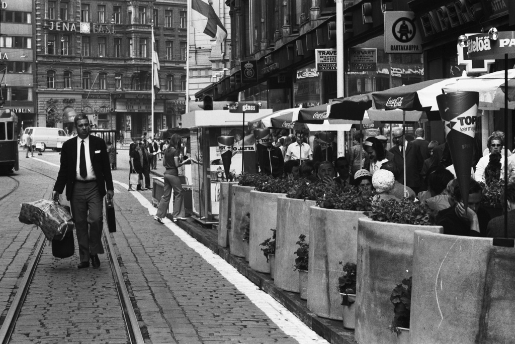 Aleksanterinkatu 21. Mies kävelemässä kantamuksineen Tallbergin talon edustalla olevan katukahvilan ohi Aleksanterinkadun kävelykatukokeilun avajaispäivänä.