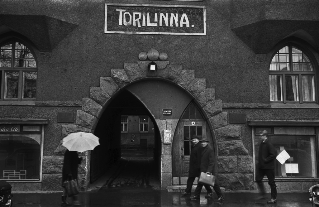Fabianinkatu 13. Ihmisiä kävelemässä sateisella Fabianinkadulla jugendtalo Torilinnan sisäänkäynnin ja porttikäytävän edustalla Kasarmitorin laidalla.