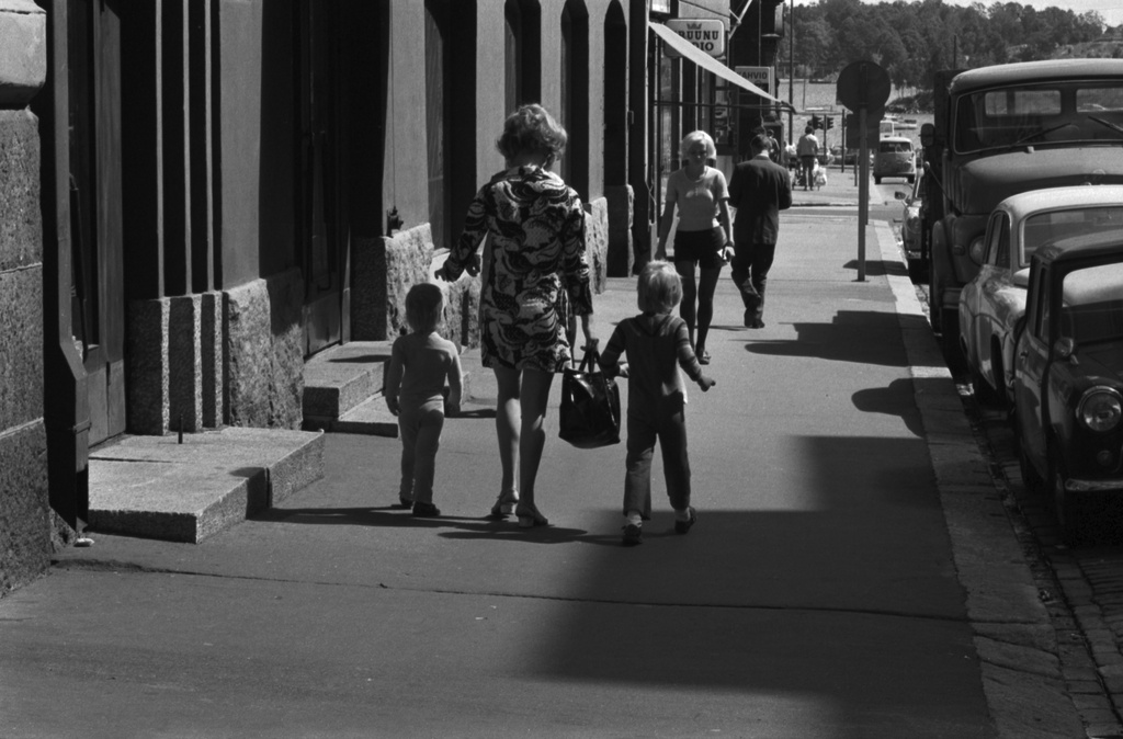 Liisankatu 5. Nainen kuviollisessa, lyhyessä leningissä kahden lapsen kanssa kävelemässä Liisankadulla.