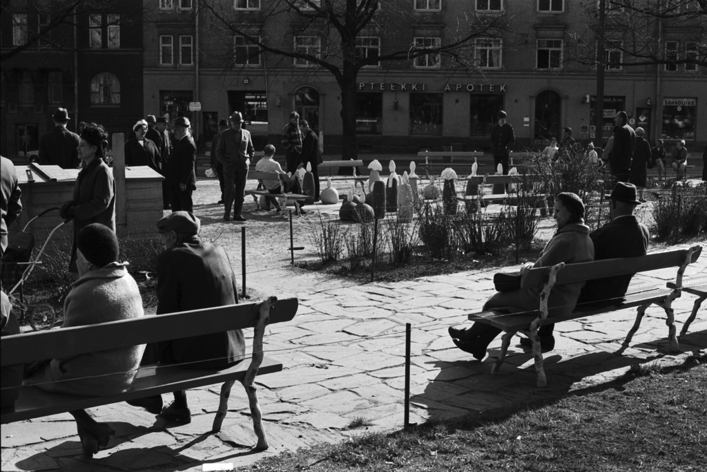 Karhupuisto. Ihmisiä puistotapahtuman aikaan aurinkoisessa Karhupuistossa, etualalla puistonpenkeillä istumassa, taustalla suuren shakkilaudan äärellä.