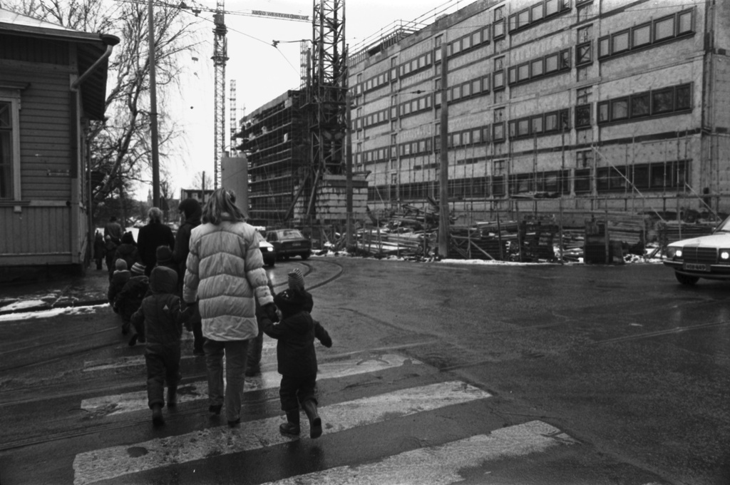 Wallininkatu 2. Vironniemen päiväkodin lapsia ja aikuisia ylittämässä Toista linjaa Wallininkadun kulmassa matkalla tutustumaan oikealla olevaan Suomen Kaupunkiliiton toimitalon (Kuntatalon) rakennustyömaahan
