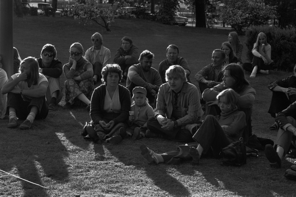 Yleisöä istumassa nurmikolla Kaisaniemenpuistossa järjestetyssä tilaisuudessa.
