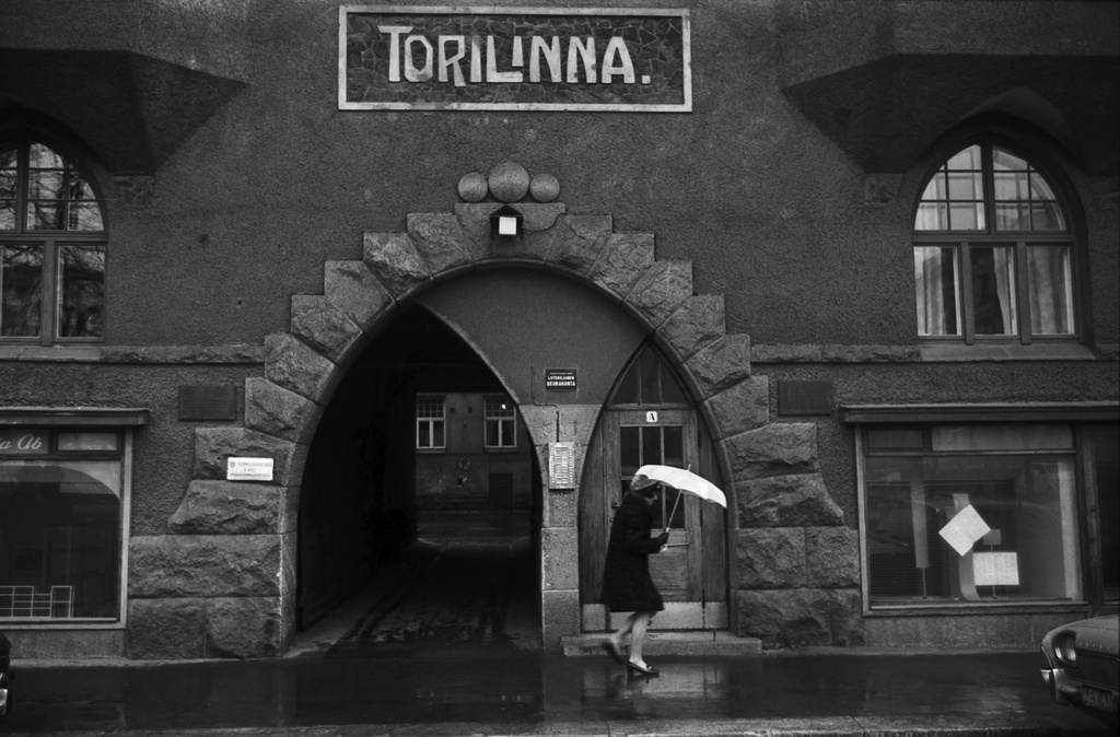 Fabianinkatu 13. Nainen kävelemässä sateisella Fabianinkadulla jugendtalo Torilinnan sisäänkäynnin ja porttikäytävän edustalla Kasarmitorin laidalla.