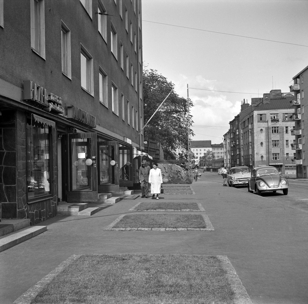 Jalankulkijoita Taka-Töölössä Ruusulankatu 8:n edustalla. Oikealla jugendtalo Ruusulankatu 17 - Sibeliuksenkatu 3. Etummainen auto Volkswagen, takana Plymouth (vm. 1954).